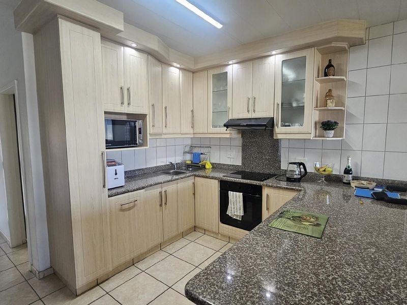 A functional kitchen featuring light wood cabinetry, granite countertops, a built-in oven, hob, and extractor fan with tiled flooring and backsplash.