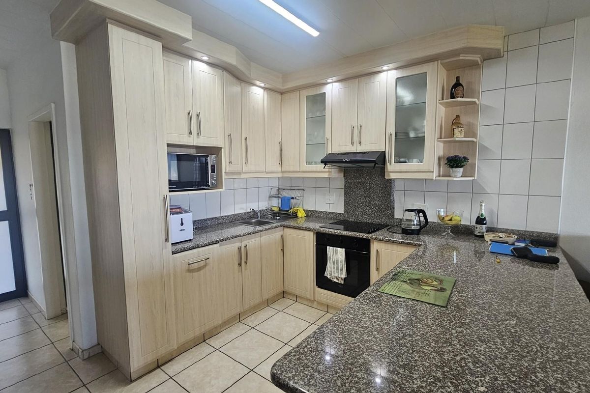 A functional kitchen featuring light wood cabinetry, granite countertops, a built-in oven, hob, and extractor fan with tiled flooring and backsplash.