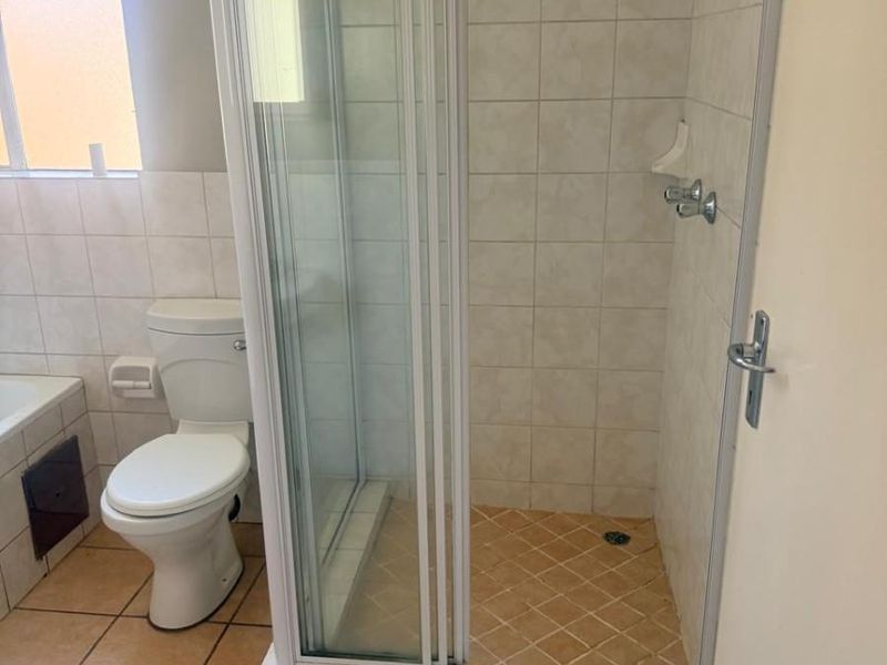 A functional bathroom featuring a glass-enclosed shower, toilet, and tiled finishes throughout, offering a clean and practical layout.