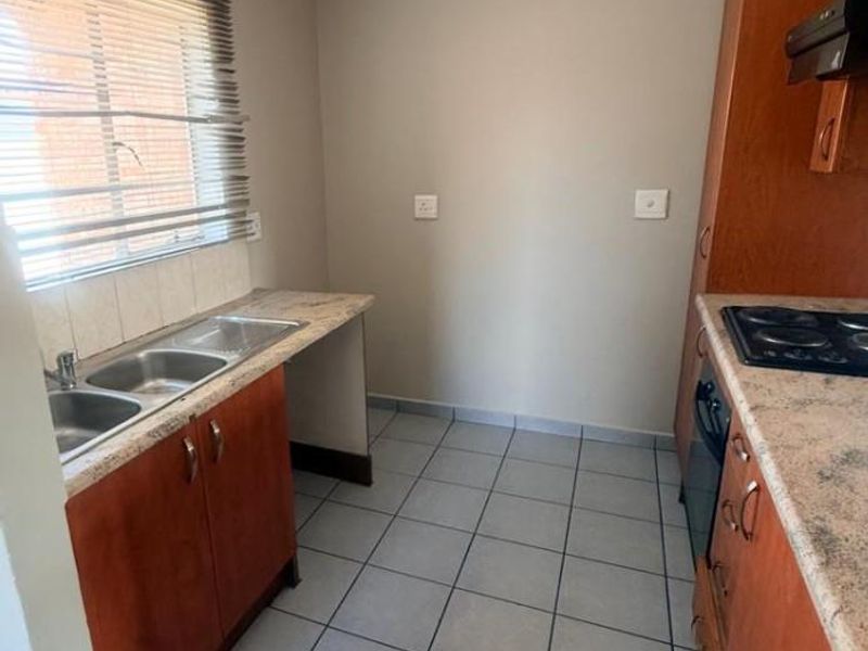 A functional kitchen featuring wooden cabinetry, laminate countertops, a double sink, and built-in cooking appliances with tiled flooring.