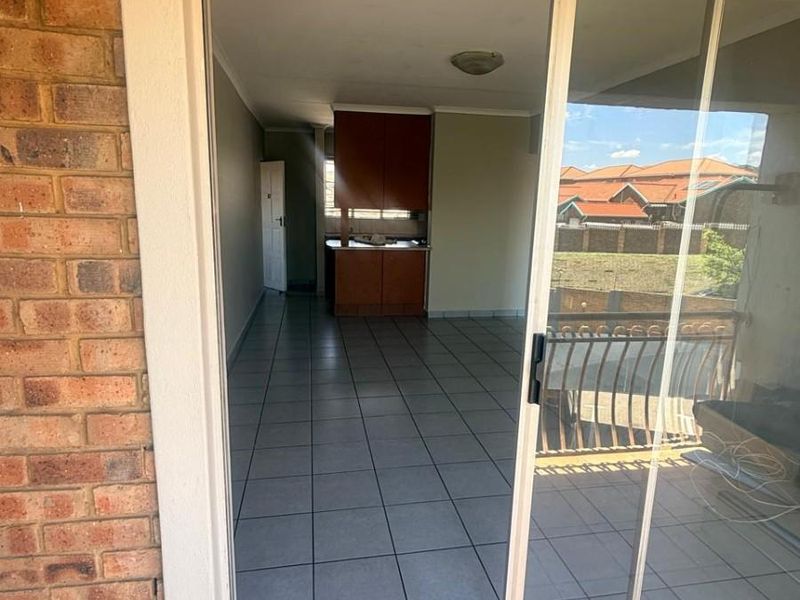 An open-plan living area featuring tiled flooring and built-in kitchen cabinetry, accessible via a sliding glass door from the patio.