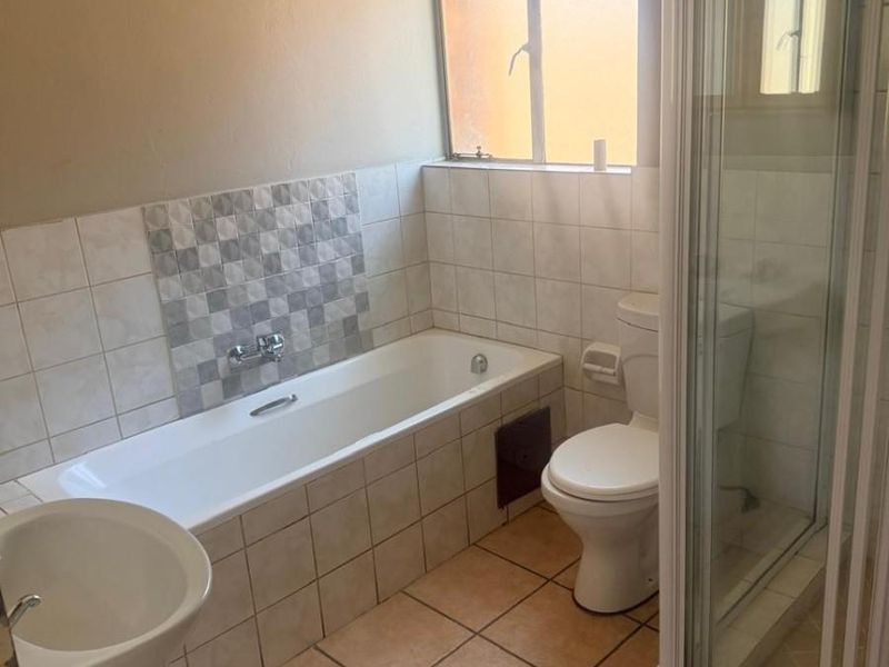 A functional bathroom featuring a bathtub, separate shower enclosure, pedestal basin, and toilet with neutral tiled finishes.
