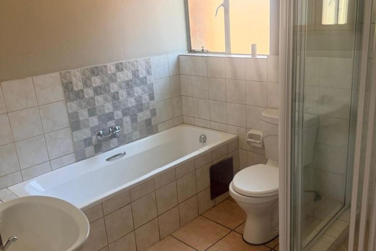 A functional bathroom featuring a bathtub, separate shower enclosure, pedestal basin, and toilet with neutral tiled finishes.
