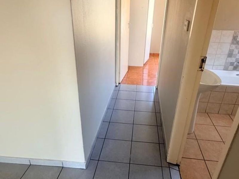 A functional hallway featuring neutral tiled flooring, connecting to adjacent rooms including a bathroom with visible tiling.