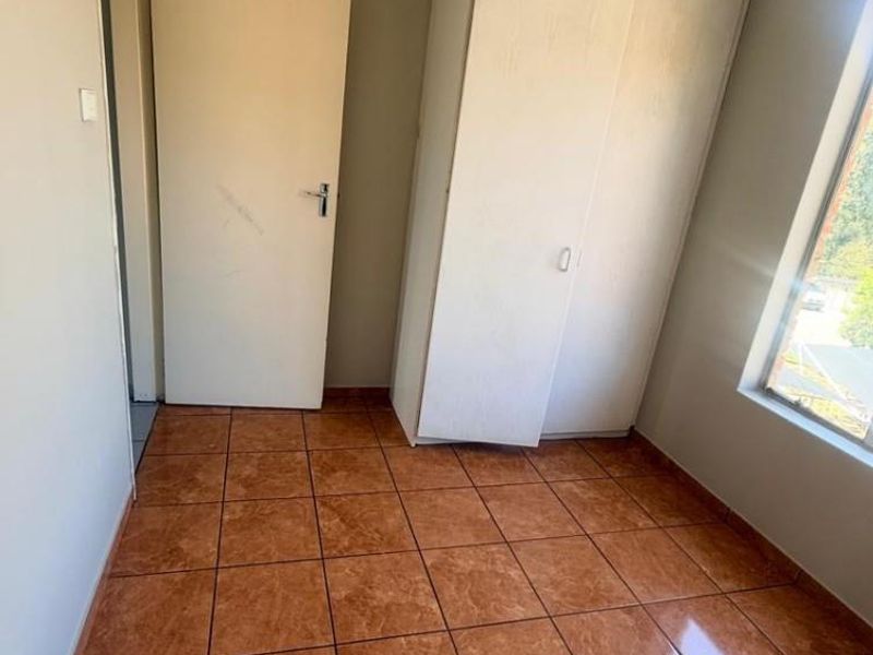 A vacant bedroom featuring tiled flooring, a built-in wardrobe, and natural light from a side window.
