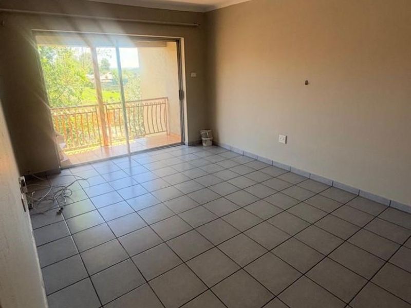 An empty living room featuring tiled flooring and a sliding glass door that opens onto a balcony, providing natural light.