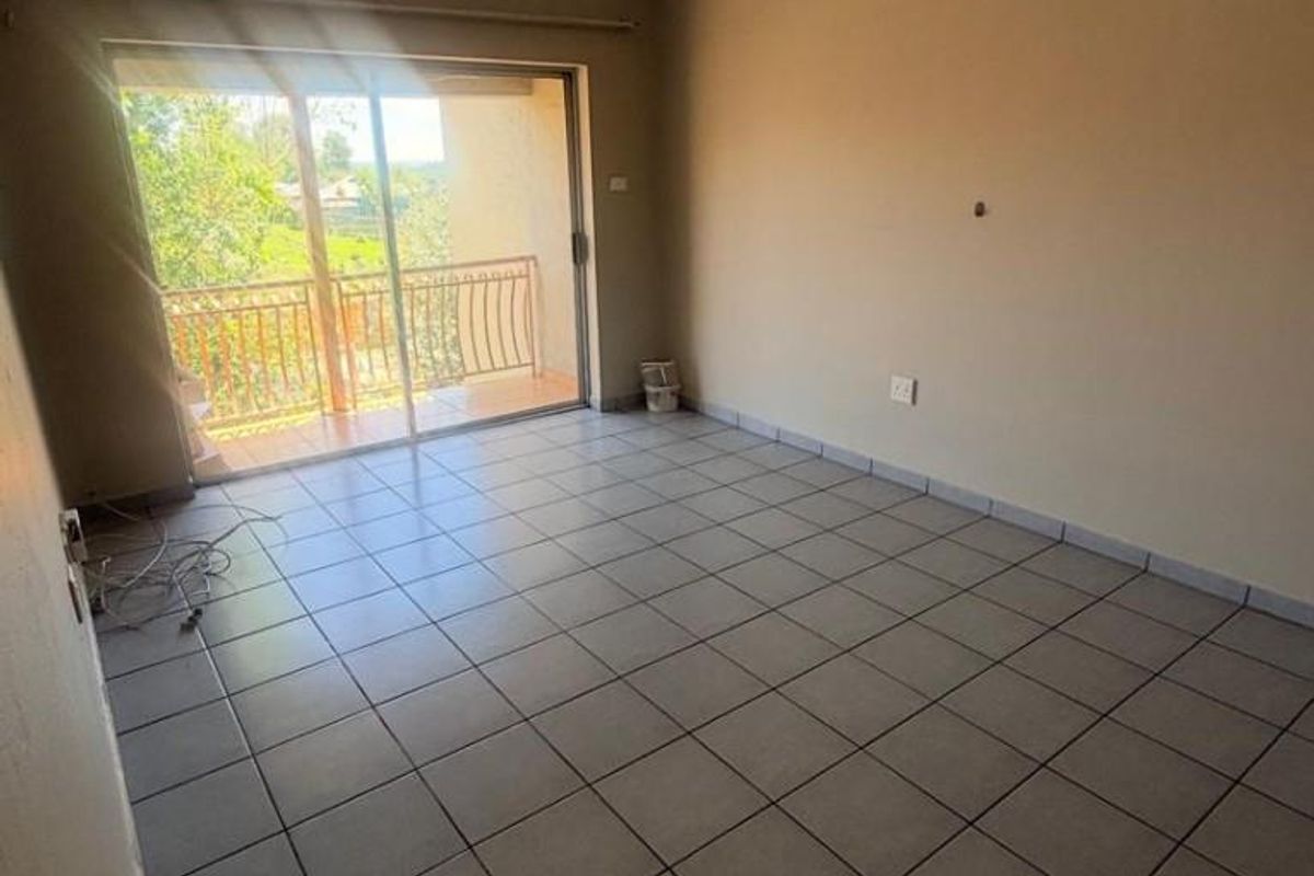 An empty living room featuring tiled flooring and a sliding glass door that opens onto a balcony, providing natural light.