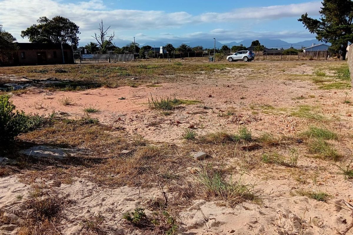 A vacant residential plot featuring sandy terrain, perimeter fencing, and mature trees, offering a blank canvas for future development.