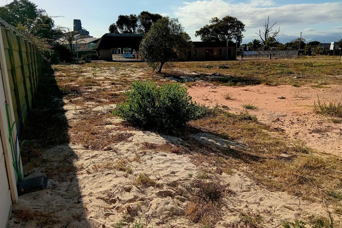 A view of a vacant residential plot featuring sandy terrain, sparse vegetation, and a boundary wall, offering potential for future development.
