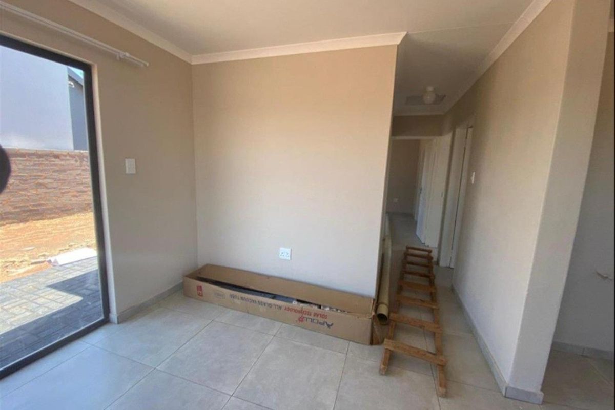 A bright, empty living area featuring neutral tiled flooring, coved ceilings, and a sliding glass door providing direct access to the exterior.