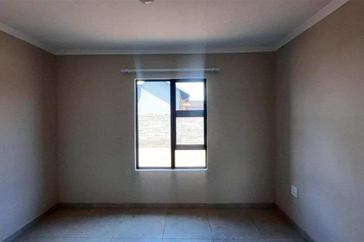 A neutral, empty bedroom featuring tiled flooring, a central window with a curtain rod, and simple cornice detailing.