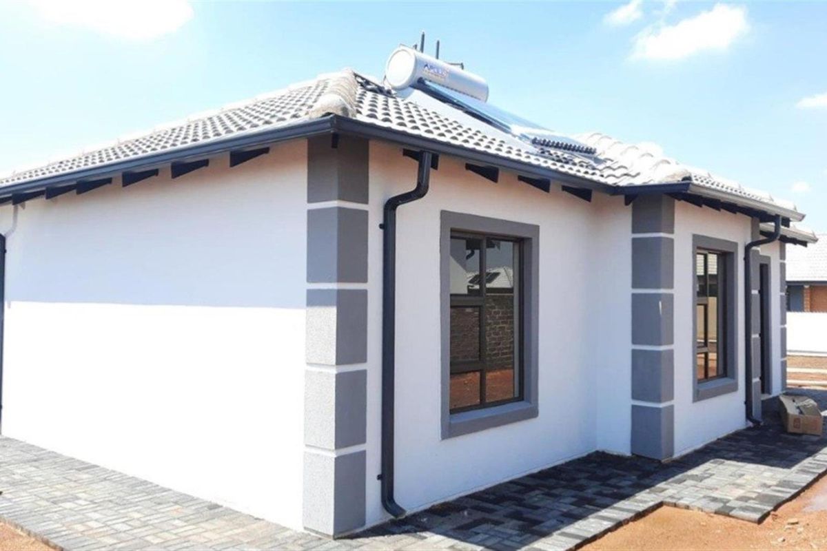 A modern single-story house exterior featuring a tiled roof, solar water heating system, paved walkways, and clean rendered facade finishes.