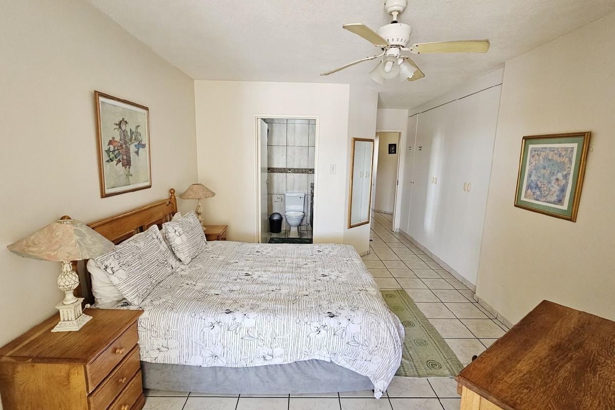 Spacious bedroom featuring built-in cupboards, tiled flooring, a ceiling fan, and an en-suite bathroom.