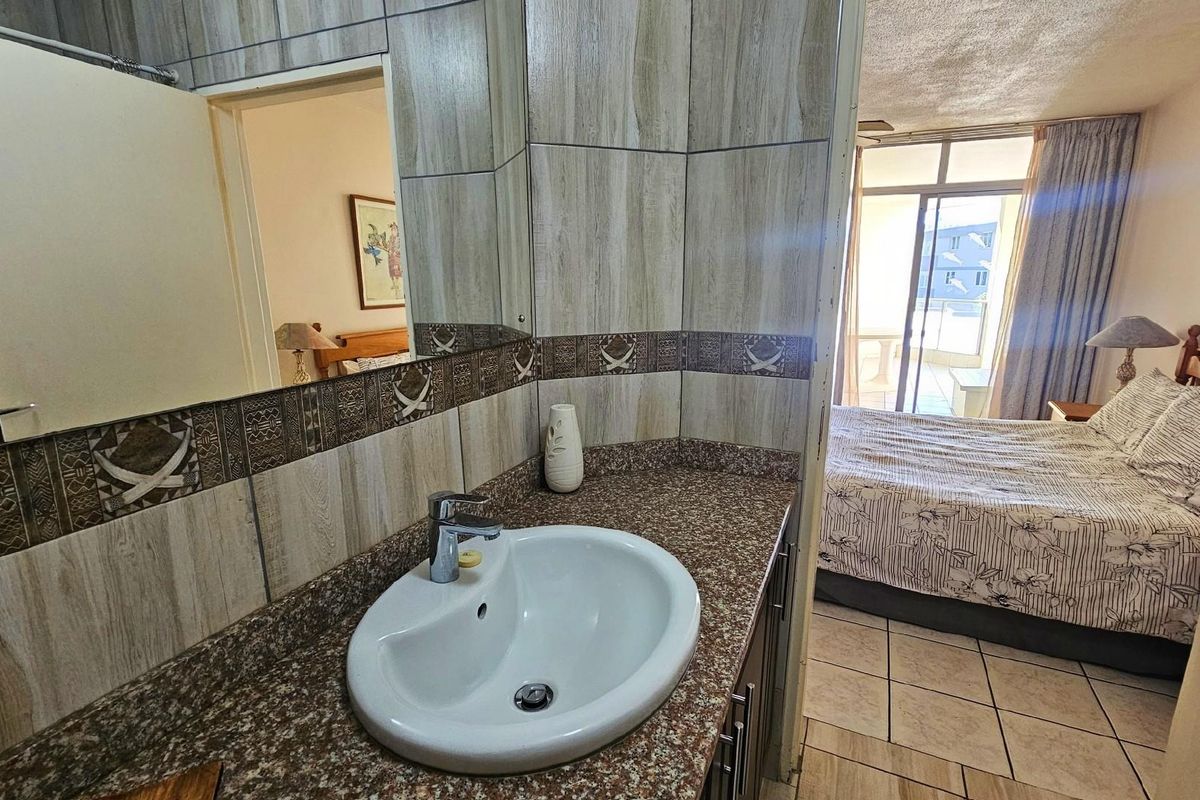 A bathroom vanity area featuring a granite countertop and integrated basin, adjacent to a bedroom with access to a balcony.