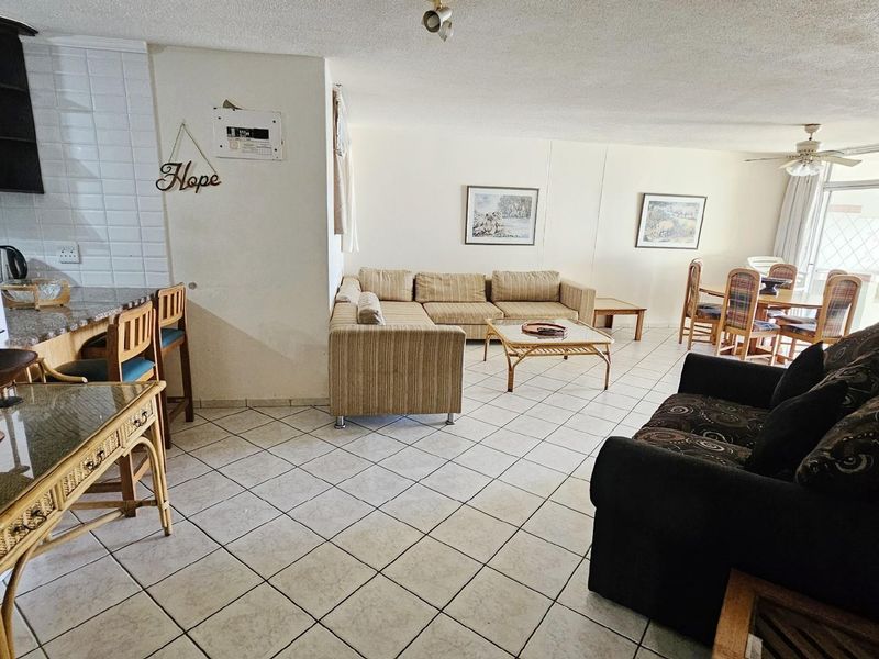 Open-plan living and dining area featuring tiled flooring, integrated kitchen breakfast bar, and direct access to a balcony.