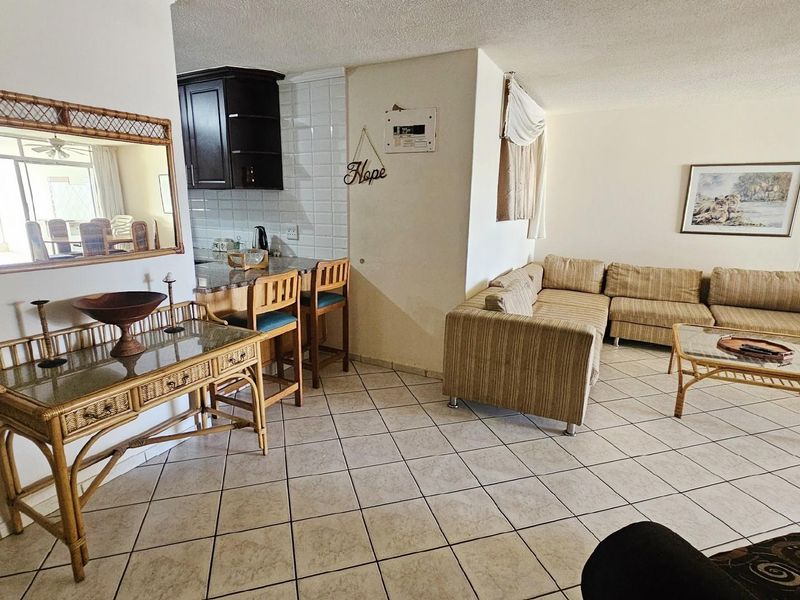 Open plan living and kitchen area featuring tiled flooring, dark wood cabinetry, and a breakfast bar, creating a functional and connected living space.