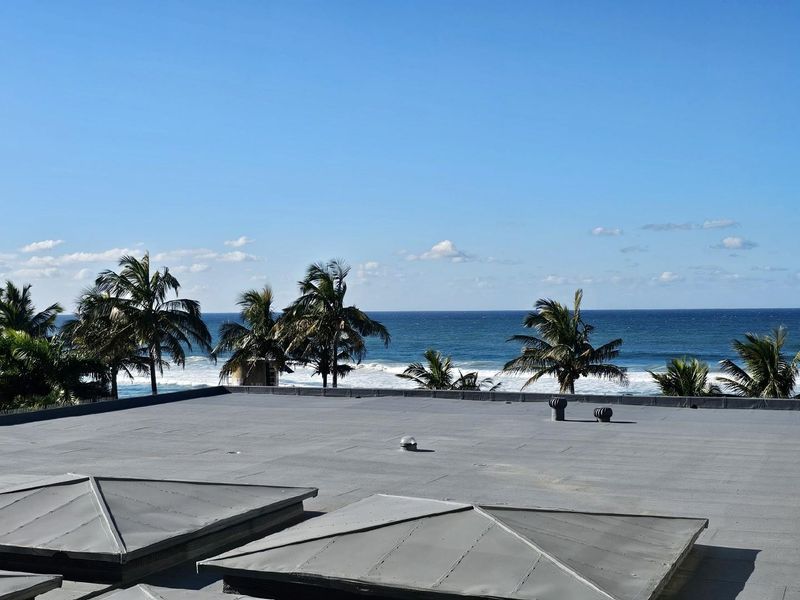 A view from the rooftop overlooking the ocean, featuring flat roofing surfaces and ventilation fixtures.