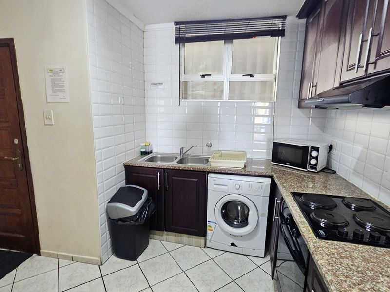 Compact kitchen featuring dark wood cabinetry, granite countertops, subway tile backsplash, integrated electric hob, and space for a front-loading washing machine.