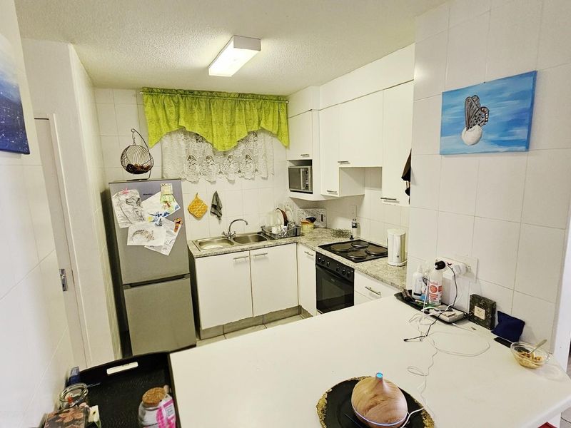 Compact kitchen featuring white cabinetry, granite-look countertops, a built-in oven, and a hob, with a breakfast bar overlooking the living area.