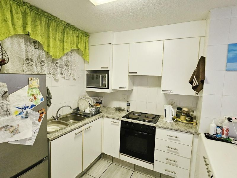 Compact kitchen featuring white cabinetry, granite-look countertops, a built-in oven with electric hob, and a double-basin stainless steel sink.