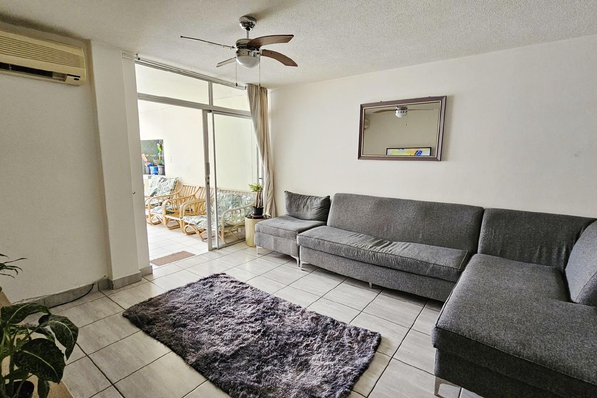 A living room featuring tiled flooring, a ceiling fan, and a wall-mounted air conditioning unit, with sliding glass doors leading to an outdoor patio area.