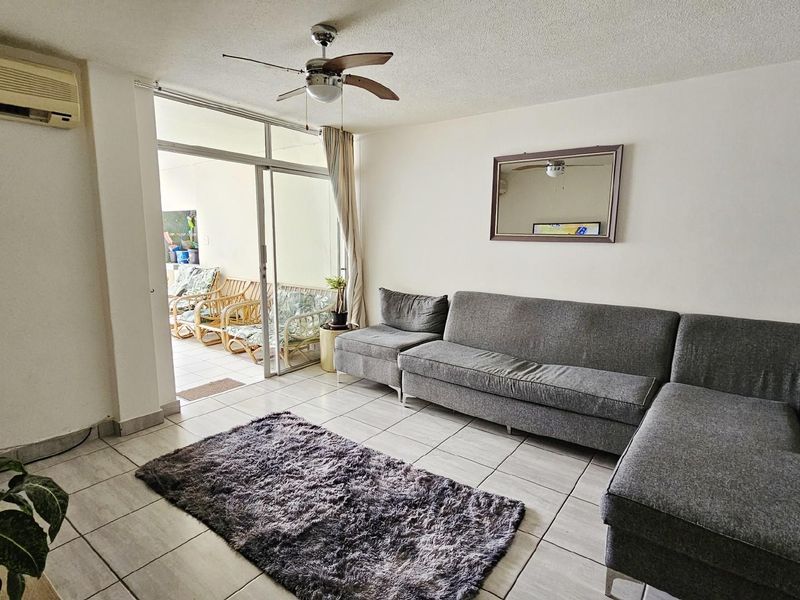 A living room featuring tiled flooring, a ceiling fan, and a wall-mounted air conditioning unit, with sliding glass doors leading to an outdoor patio area.