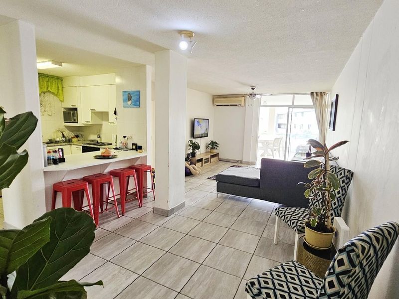 Open-plan living area featuring a functional kitchen with breakfast bar, tiled flooring, and direct access to a private balcony.