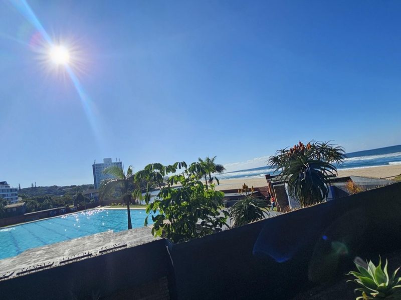 A scenic view of the communal swimming pool area overlooking the beach and ocean, showcasing the property's coastal location.