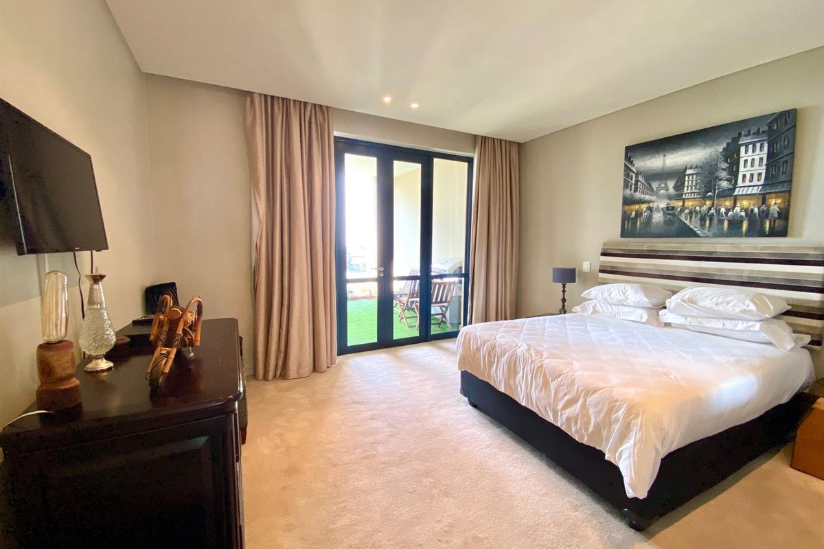A spacious bedroom featuring neutral carpeting, recessed ceiling lighting, and large glass doors providing direct access to a private balcony.