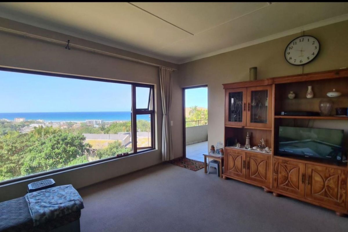 Spacious living room featuring a large picture window with expansive ocean views and direct access to an outdoor balcony area.