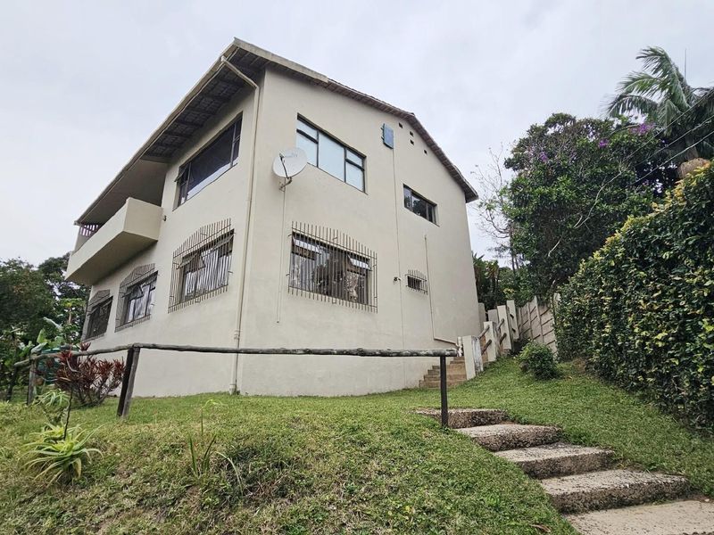 Exterior view of a multi-story residential house featuring a balcony, security bars on windows, and a landscaped garden with concrete steps.