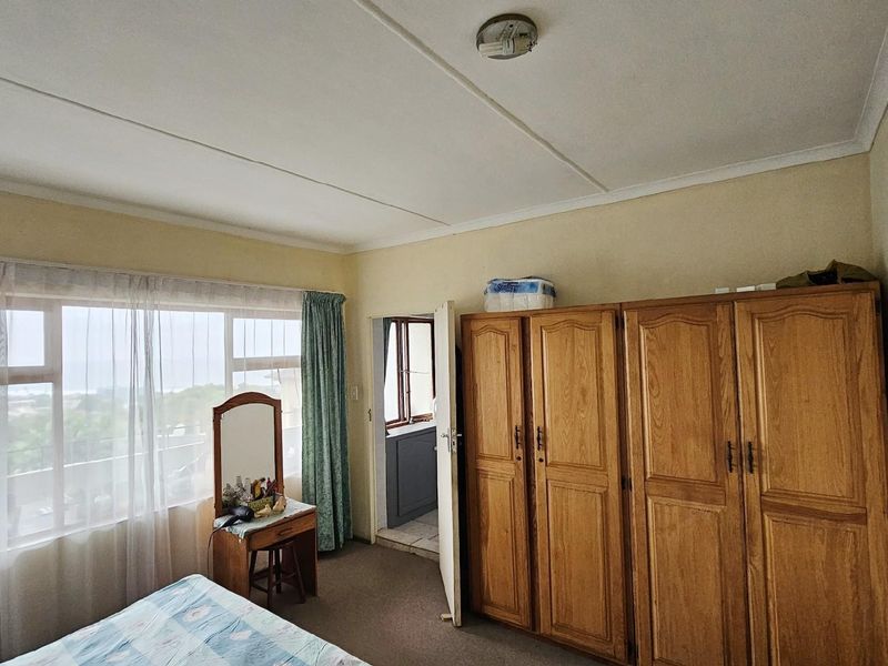 A bedroom featuring large windows with natural light, built-in wooden cabinetry, and carpeted flooring, offering a functional space with potential for modernization.