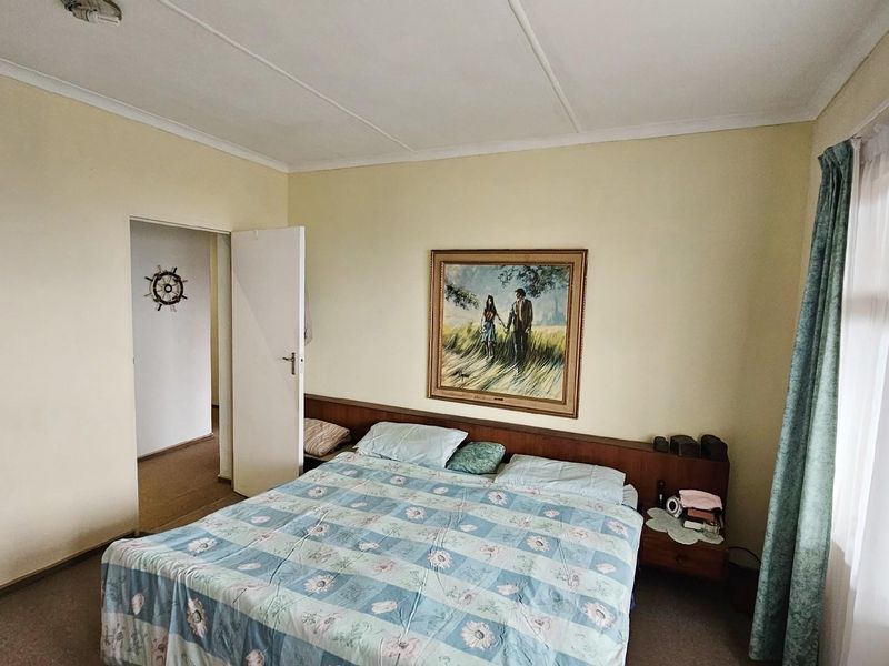 A bedroom featuring built-in headboard cabinetry, carpeted flooring, and access to an adjoining hallway.