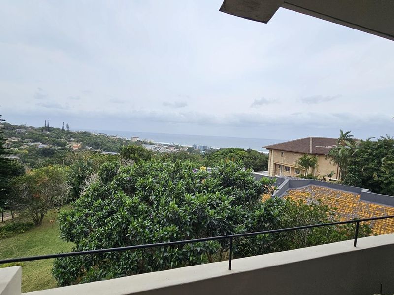 Elevated balcony view overlooking the surrounding neighborhood, lush greenery, and distant ocean coastline.