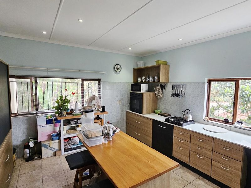 Functional kitchen featuring wood-look cabinetry, built-in oven, gas hob, tiled splashbacks, and a central island workspace with integrated storage.