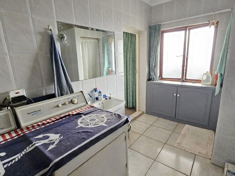 Functional laundry room featuring tiled walls and flooring, built-in storage cabinetry, a basin, and dedicated space for laundry appliances.