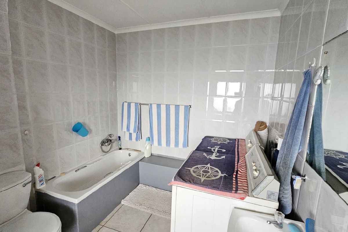 A functional bathroom featuring a built-in bathtub, toilet, and wall-mounted vanity mirror with full-height wall tiling.