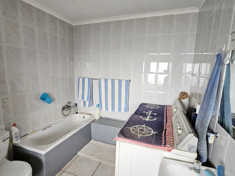 A functional bathroom featuring a built-in bathtub, toilet, and wall-mounted vanity mirror with full-height wall tiling.