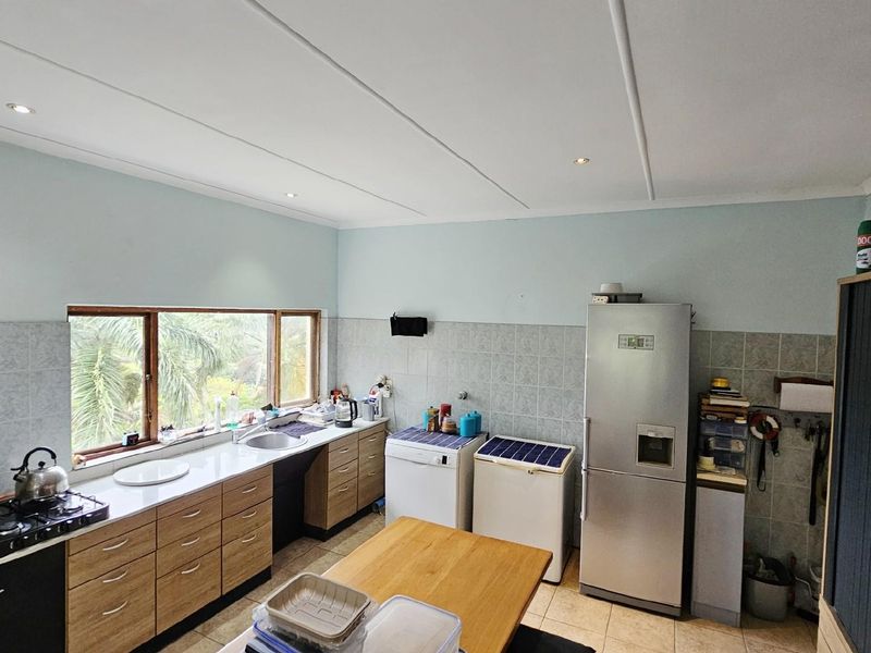 A functional kitchen featuring wood-look cabinetry, tiled splashbacks, a built-in gas hob, and a large window providing natural light and garden views.