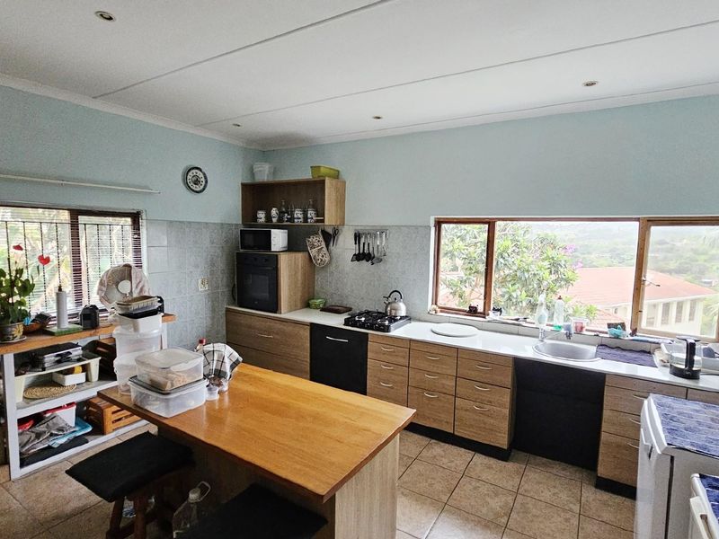 Functional kitchen featuring wood-tone cabinetry, built-in oven, gas hob, and tiled countertops with a double sink and large windows overlooking the garden.