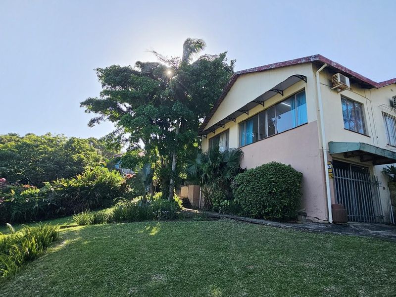 Exterior view of the property featuring a sloped lawn, mature garden, and multi-level building facade with security bars and wall-mounted air conditioning units.