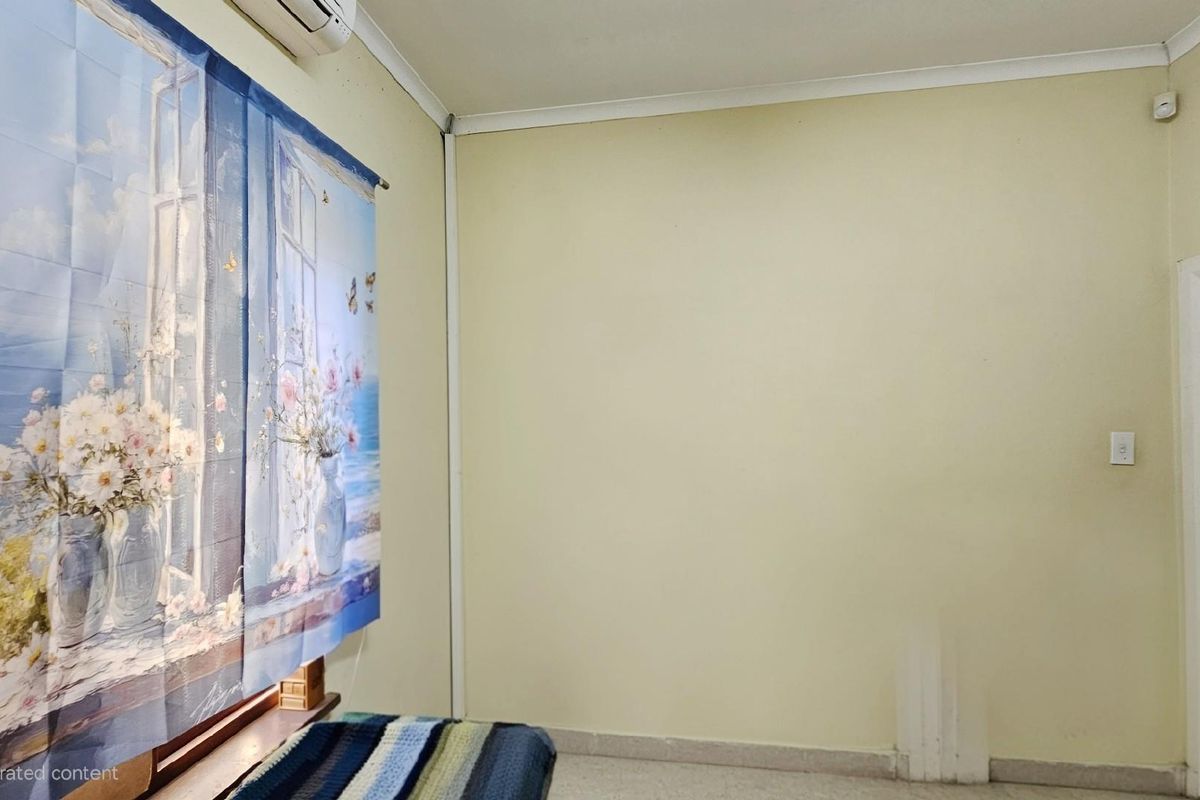 A sparsely furnished bedroom featuring a wall-mounted air conditioning unit, coving, and a doorway leading to an adjacent space.