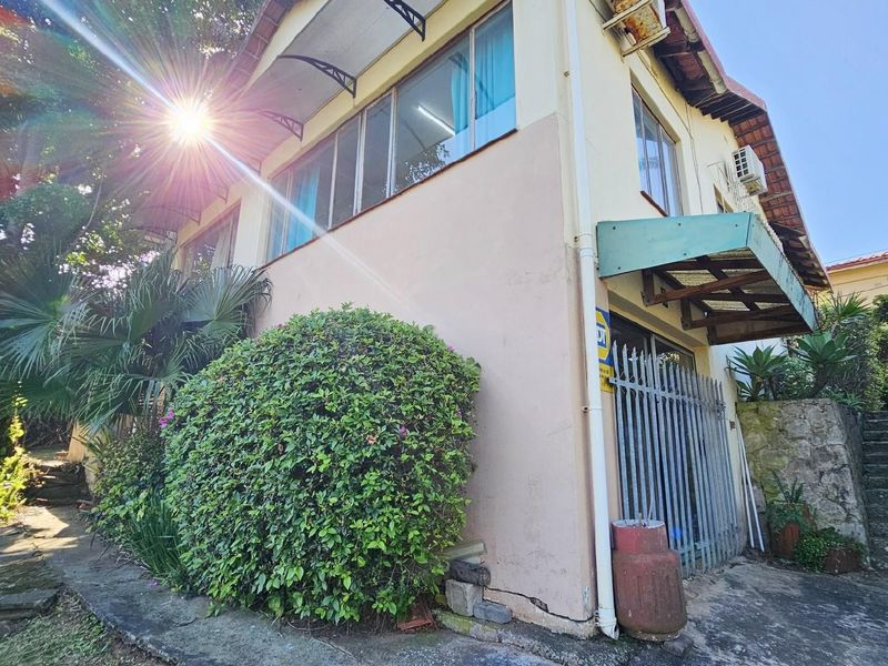 Exterior view of the property featuring a multi-level facade, metal security gate, and stone staircase leading to the upper garden area.