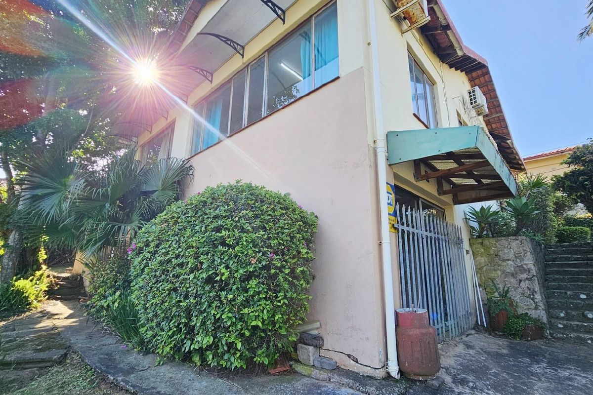 Exterior view of the property featuring a multi-level facade, metal security gate, and stone staircase leading to the upper garden area.