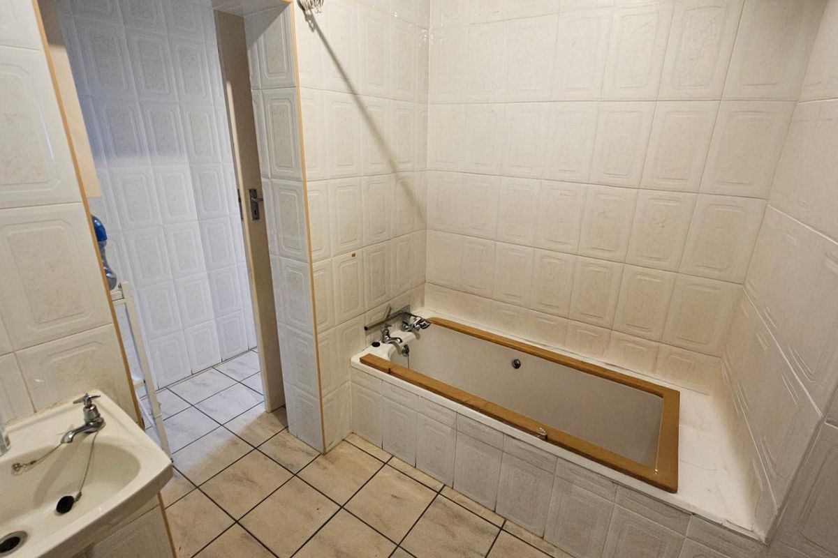 A dated bathroom featuring a built-in bathtub with tiled surround, a pedestal basin, and full-height wall tiling.