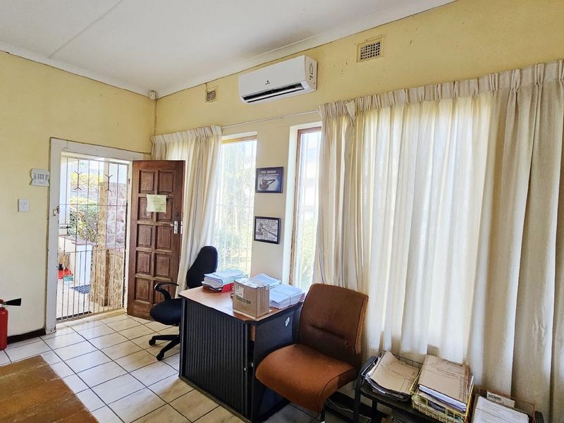 A functional office space featuring tiled flooring, a wall-mounted air conditioning unit, and direct access to an exterior area.