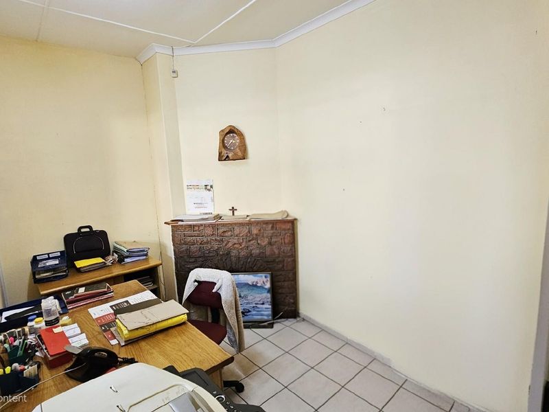 A functional office space featuring a corner fireplace with a brick-style finish and tiled flooring, suitable for a home workspace or study.