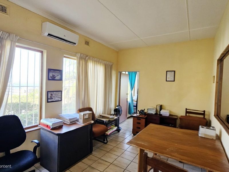 A functional office space featuring tiled flooring, large windows with security bars, and a wall-mounted air conditioning unit.