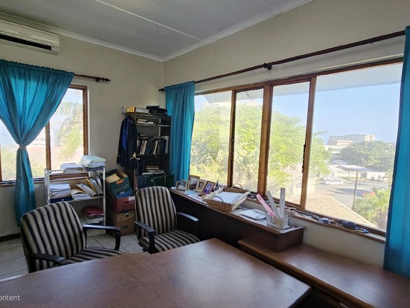 A functional home office space featuring large windows with natural light, tiled flooring, and a wall-mounted air conditioning unit.