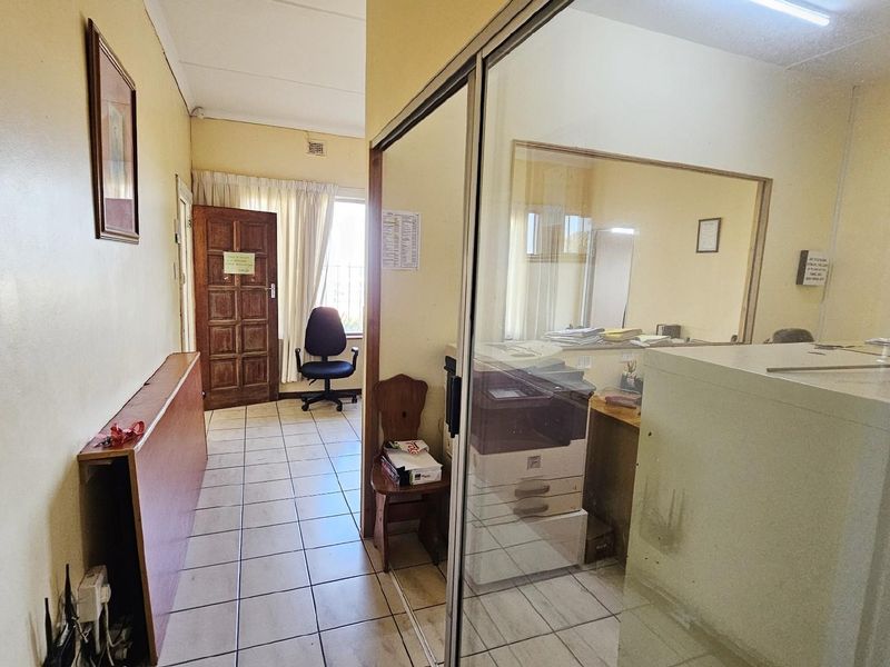 A functional office space featuring tiled flooring, a glass partition wall, and a solid timber entrance door.